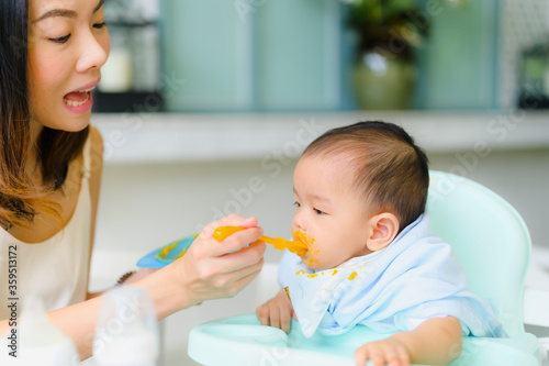 Asian 7 months baby boy eating blend food on a high chair, Mother  feeds a Little Baby with a Spoonful of food.