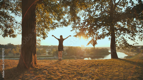 The girl enthusiastically runs to meet the sunset on the background of the city and raises her hands. Video in motion.