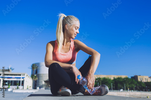 Portrait of an attractive female jogger with cute smile enjoy rest after workout against blue sky with copy space for your text message or content, young fit woman in sportswear taking break after run