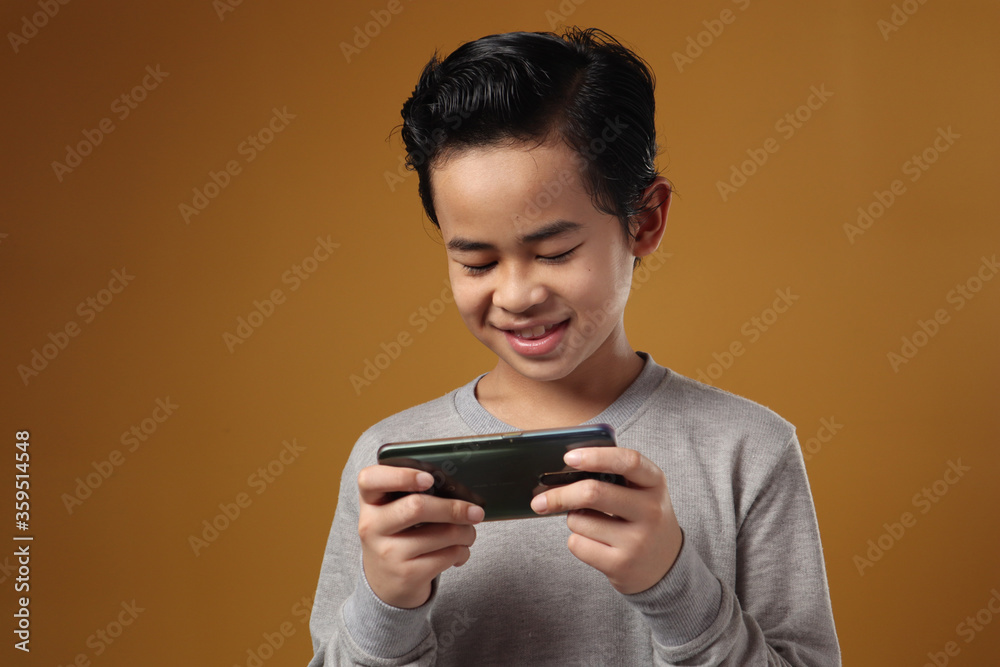 Portrait of Asian boy plays online game on his phone, smiling happy face, kid with gadget