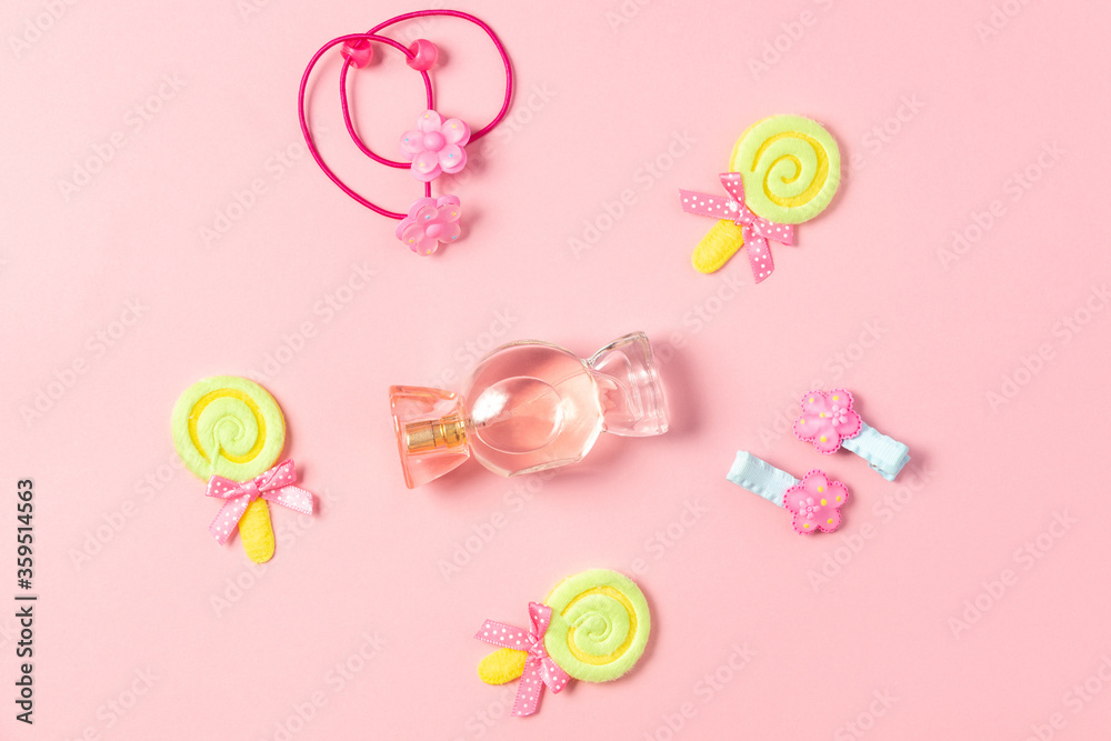 Children's flat lay. Perfume in the form of candy, children's jewelry and hair accessories on a pink background. Accessories for little girls.