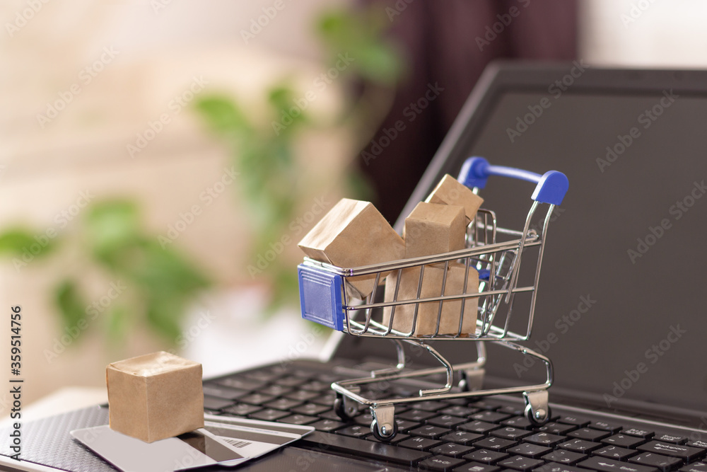 Online shopping with home delivery. Shopping basket and boxes on laptop keyboard.