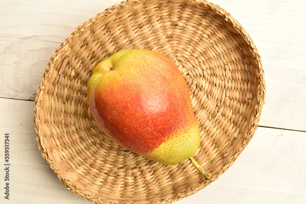 Sweet juicy pears with a straw plate on a white wooden table. Sweet juicy pears with a straw plate on a white wooden table.
