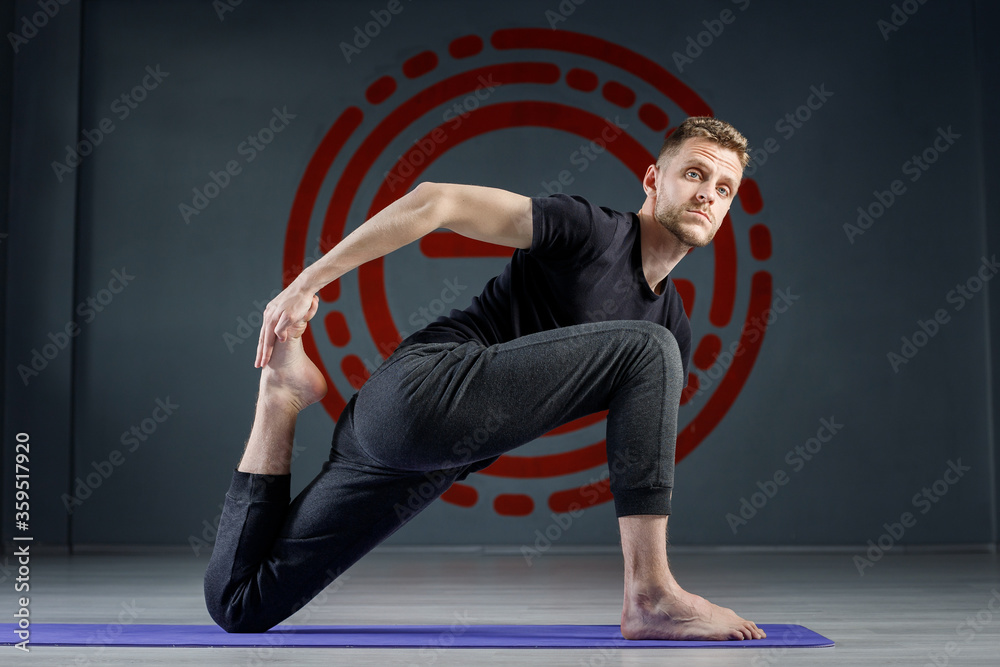 Young man doing leg stretching exercises on a yoga mat in the gym.