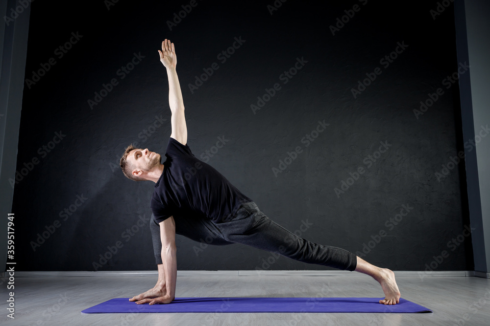 Young man doing leg stretching exercises on a yoga mat in the gym. Practising yoga positions.