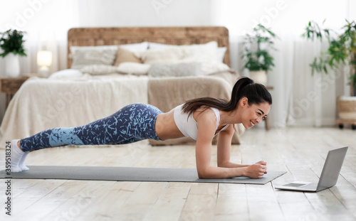 Home Exercises. Sporty asian girl doing yoga plank in front of laptop