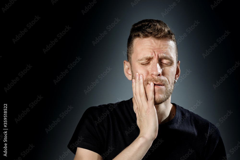 Young man, showing painfull, toothache emotions on black background.