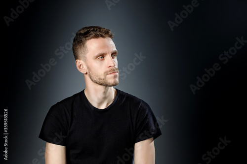 Young man, is thoughtfully looking to the side with on black background.