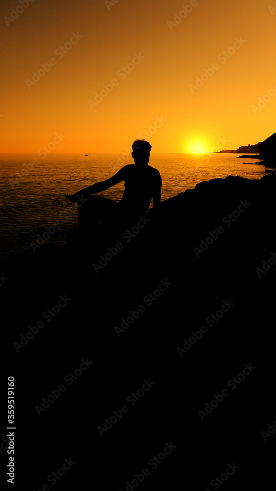 Man sitting on a rock and looks at the sea at sunset