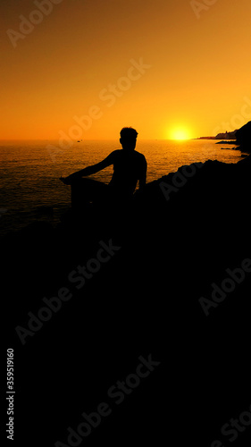Man sitting on a rock and looks at the sea at sunset