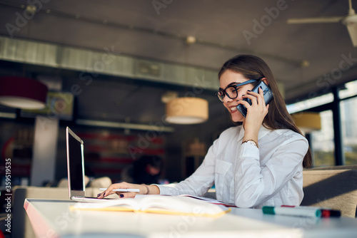 Attractive female administrative manager of restaurant arranging working meeting with staff members to discuss plans for month through telephone conversation sitting in food court using technology photo