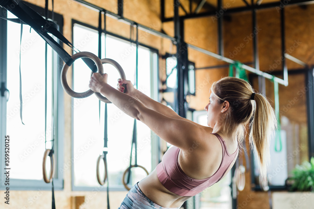 Obraz premium Young sporty woman training on gymnastic rings