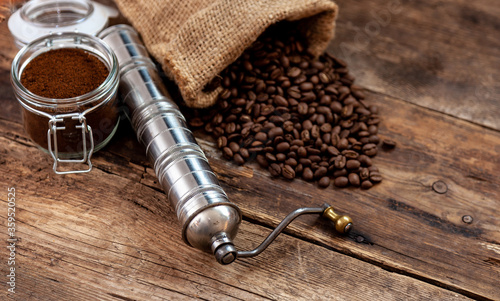 Bag of coffee on a wooden table. Coffee beans ground in a jar. Manual coffee grinder. Top view, place for text. Brown background. Packing coffee in a pack. White up with a drink.