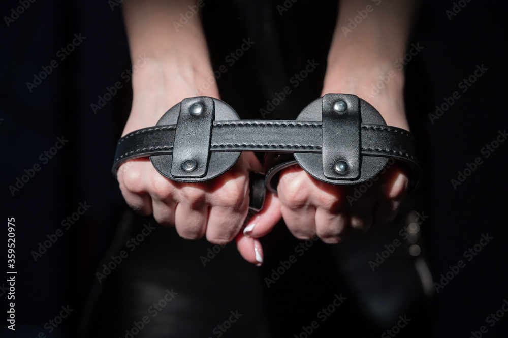 Close-up leather blindfolds in female hands. Unrecognizable woman holds bdsm equipment in the dark. Sexual role-playing games for adults. Humility and dominance.