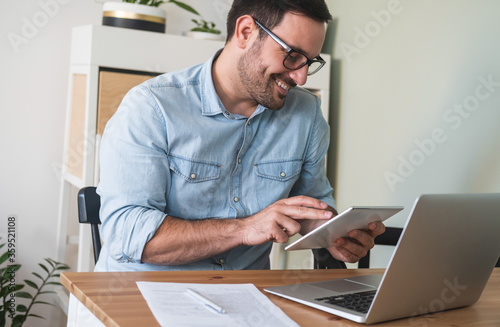 Handsome young man using digital tablet, sitting at a table with laptop and business papers stock photo