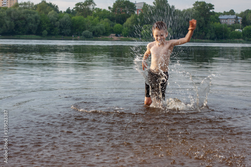 Fototapeta Naklejka Na Ścianę i Meble -  a boy splashes water in the river. bathes. children's happiness