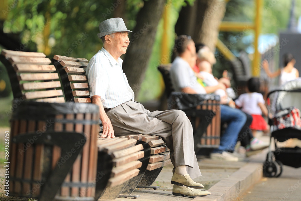 old man sits and rests on a bench in the summer