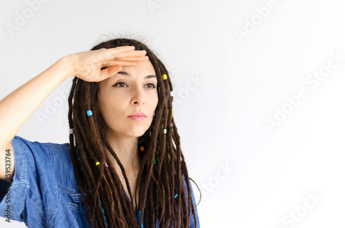 beautiful girl with dreadlocks looks into the distance covering her eyes with her hands