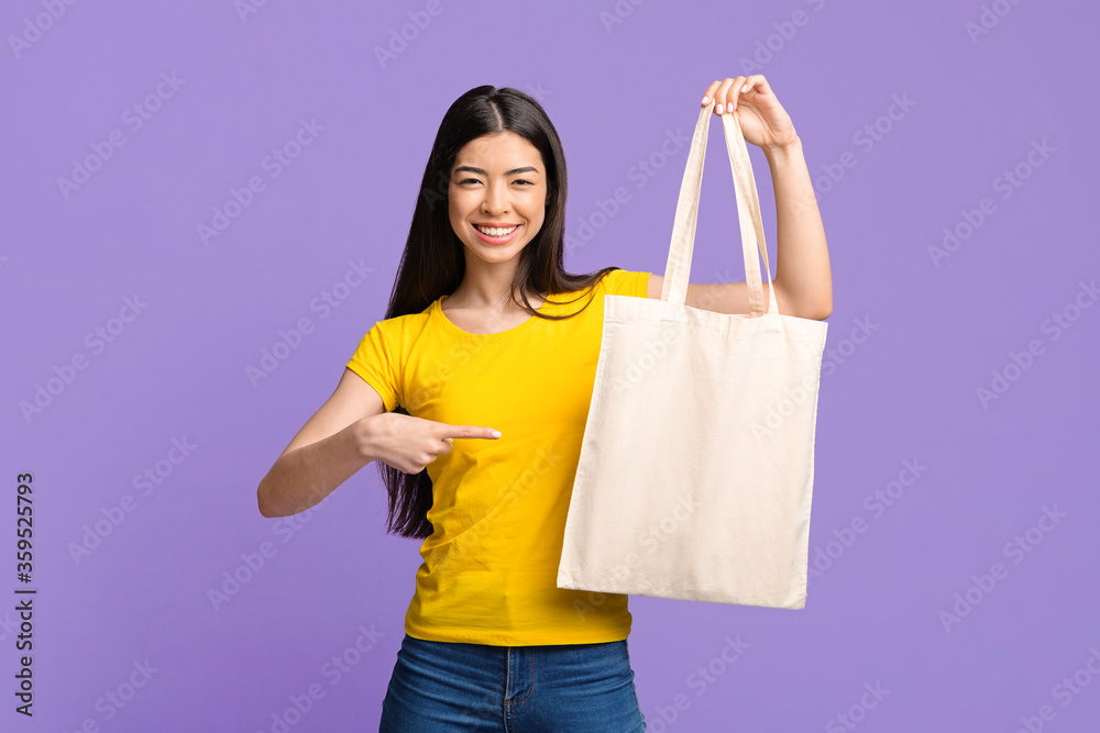 Mockup For Your Design. Joyful Asian Girl Pointing At Blank Tote Bag Mockup For Your Design. Joyful Asian Girl Pointing At Blank Tote Bag