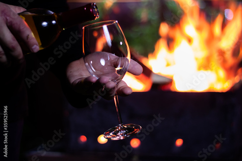 pour a glass of white wine from a bottle on the background of a barbecue with fire