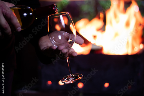pour a glass of white wine from a bottle on the background of a barbecue with fire