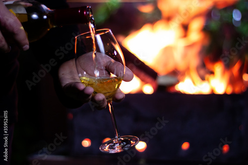 pour a glass of white wine from a bottle on the background of a barbecue with fire
