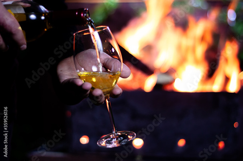 pour a glass of white wine from a bottle on the background of a barbecue with fire