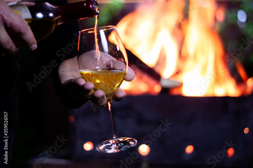 pour a glass of white wine from a bottle on the background of a barbecue with fire
