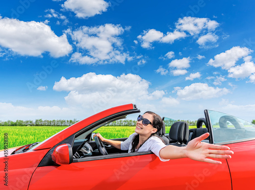 Woman in a red car against the background of a field and blue sky outside the city.