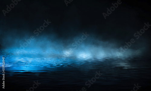 Темная улица, мокрый асфальт, отражения лучей в воде. Абстрактная синяя предпосылка, дым, смог. Пустая темная драматичная сцена, неоновый свет, прожекторы. Жидкость. Река ночью. © MiaStendal