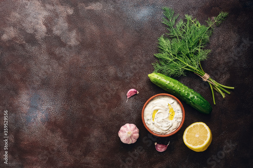 Traditional greek tzatziki sauce with ingredients on dark rustic background. Greek yogurt with cucumber, dill, garlic and lemon. Top view, copy space, flat lay.