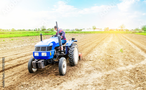 Farmer drives a tractor on a farm field. Agricultural industry. Cultivating land soil for further planting. Loosening  improving soil quality. Food production on vegetable plantations.