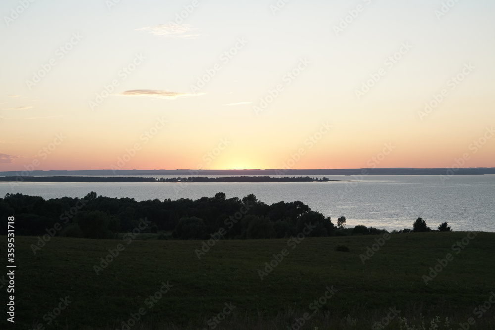 Sunset over a wide river. A summer evening background in pale Grays and pinks against a dark green background. Copy space.