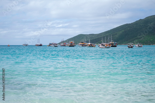 Several tourist boats in clear azure water of an ocean against a background of green mountains.