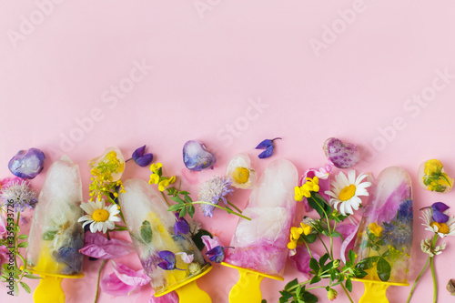 Floral Ice Pops. Colorful wildflowers in frozen popsicles and ice cubes on pink background flat lay and fresh summer flowers. Copy space. Hello summer concept. Creative bright image