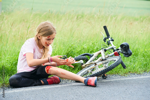 Sad crying little child girl fell from the bike in the summer park. Bleeding on hands and feet. Bicycle accident. Injuries while cycling. Accidents and injuries to children during summer activities