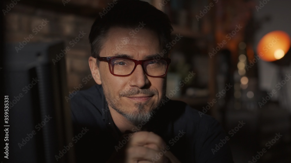 Facial portrait of mature man in his 50s at home sitting in dark living room, thinking. Facial portrait of mature man in his 50s at home sitting in dark living room, thinking.