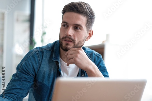 Handsome modern man designer working on laptop online, using internet at home