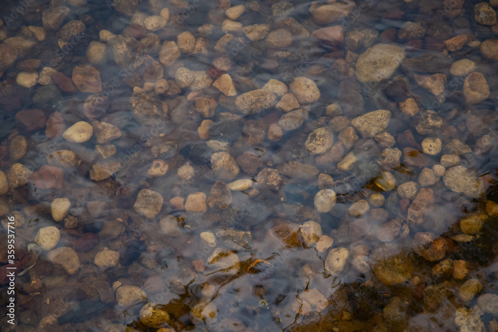 Background of stones under water. Stone pebbles under the waves of river, sea water.