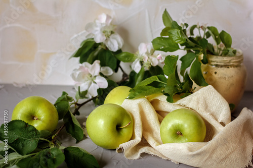 Ripe green apples and apple flowers on light fabric close-up. Horizontal photo.