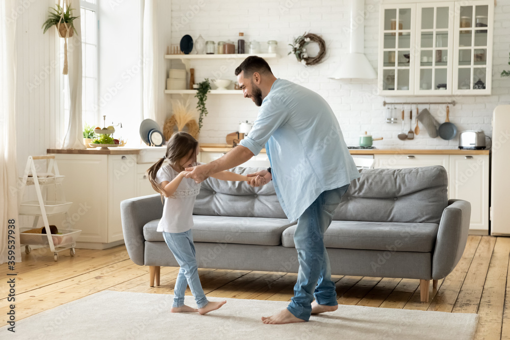 Happy father dancing having fun with little daughter in modern living room. Family playing funny game, young dad and adorable cute girl moving to favorite music enjoying weekend at home.