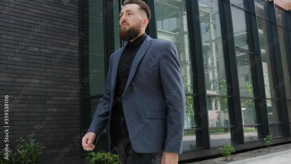 Bearded Man in a formal suit is going to the business meeting, outside, business building background Bearded Man in a formal suit is going to the business meeting, outside, business building background