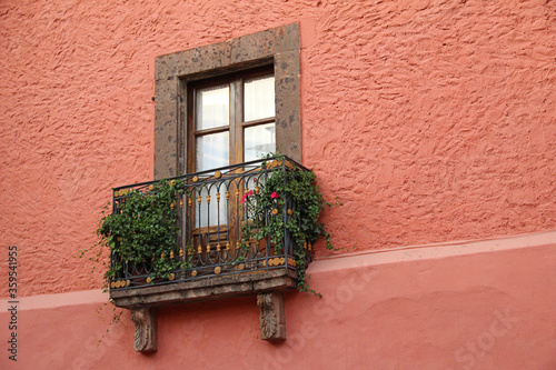 Colorida fachada colonial con Ventana barandal con flores pared color naranja rojizo arquitectura en México san Miguel de allende con cantera y detalles en madera rústica 