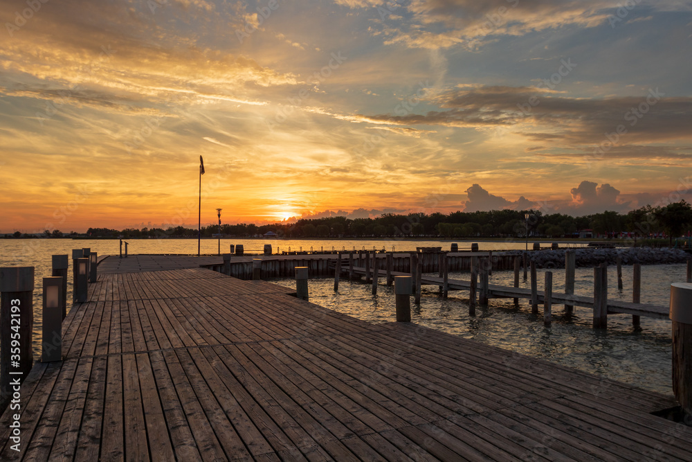 Wooden pier at Lake Neusiedl in Podersdorf, Austria. In the background is a dramatic sky at sunrise.