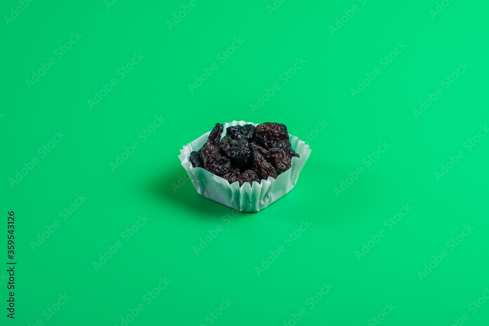 A portion of black raisins in a paper muffin cup on a green background. A portion of black raisins in a paper muffin cup on a green background.