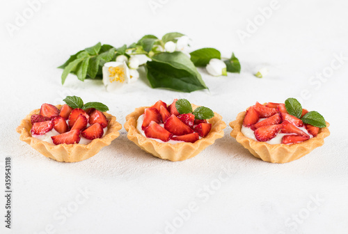 Dessert tartlets with vanilla cream and strawberries on a light background