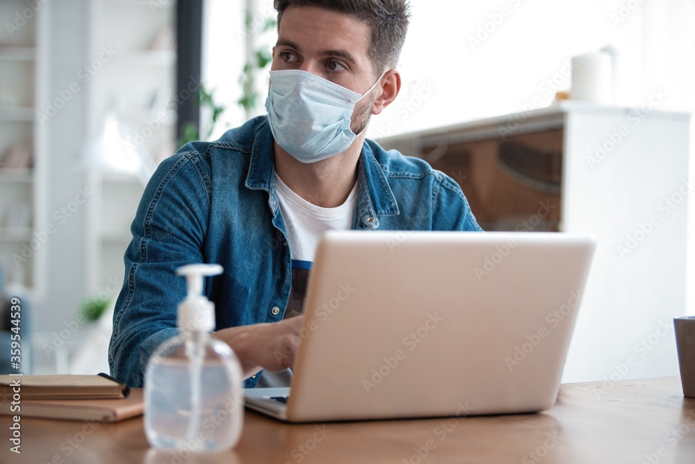 Young caucasian man working from home, wearing protective mask, using laptop. Coronavirus pandemic, covid 19 quarantine Young caucasian man working from home, wearing protective mask, using laptop. Coronavirus pandemic, covid 19 quarantine