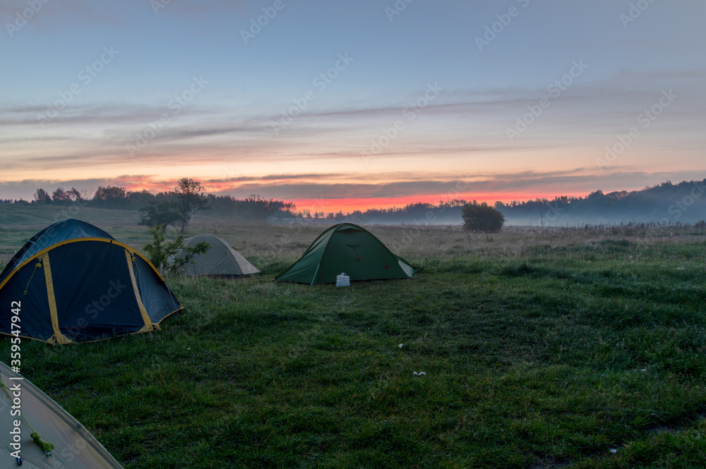 Tourist tents in the field. Tourist camp in the fog. Morning fog at sunrise.
