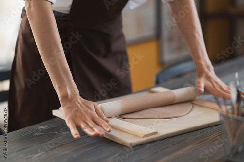 Female hands flatting piece of clay lying on fabric using wooden rolling pin in ceramic studio. photo