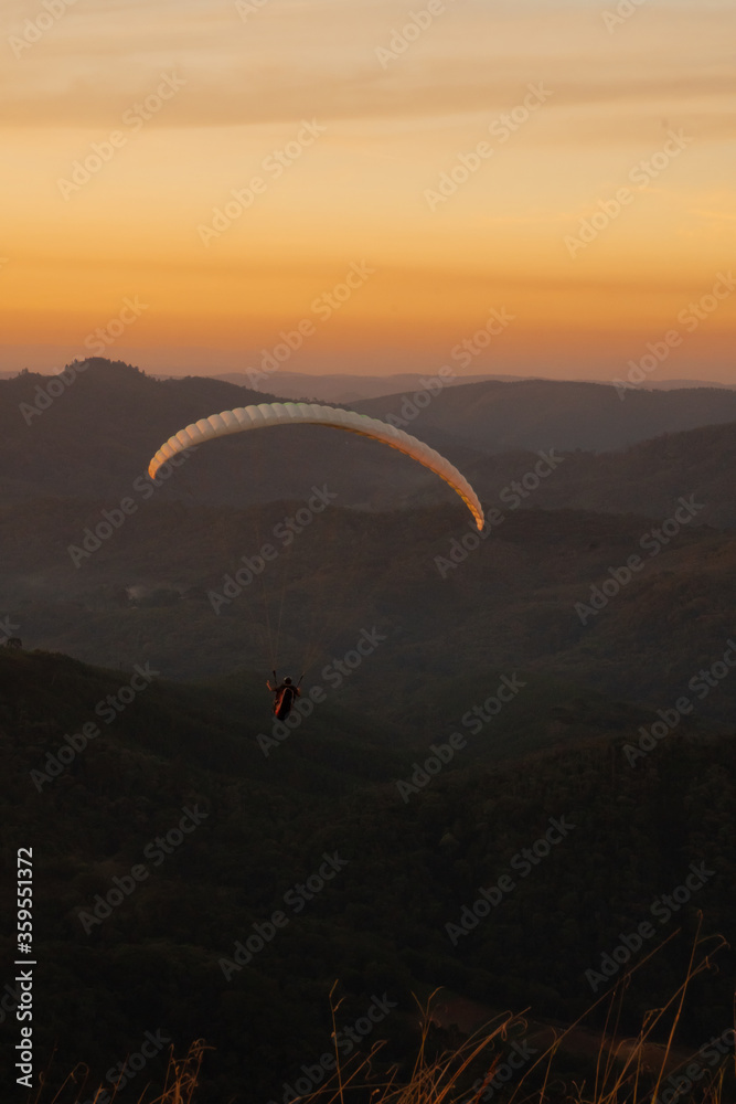 Paragliding concept, Beauty nature mountain landscape. Paraglider silhouette flying over misty mountain valley in beautiful warm sunset.
